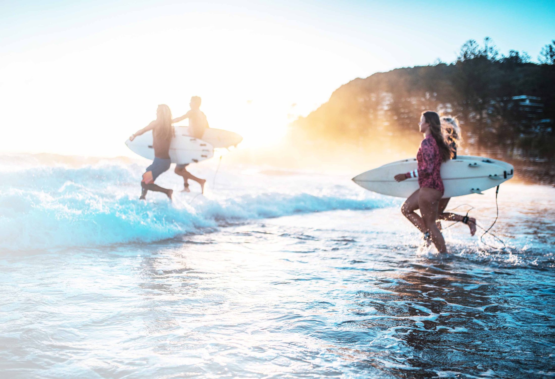 Jeunes surfeurs courant dans les vagues au coucher du soleil
